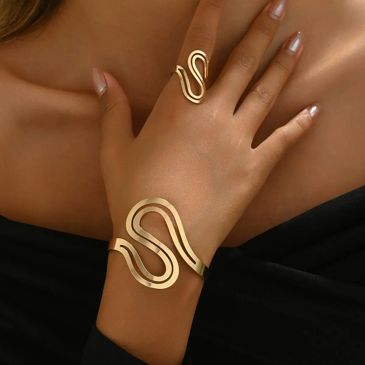 Bold serpentine wave-cut gold cuff bracelet with matching ring on model's wrist and hand